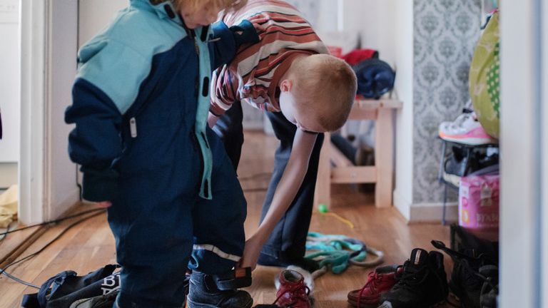 Ett foto av ett barn som hjälper ett mindre barn att ta på sig skor i en hall.