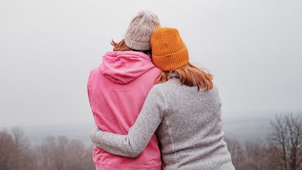 Två personer i joggingkläder håller om varandra. Man ser bara ryggarna på dem och de har mössor på sig. 