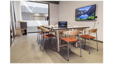 Mindre rum med bord, stolar och bildskärm. 