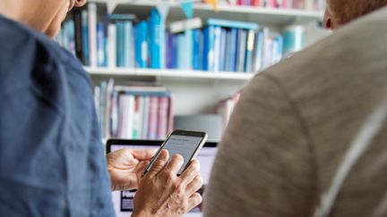 Leende person visar en annan person något på sin mobiltelefon.
