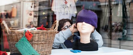 En person sätter en mössa på en skyltdocka i skyltfönstret.