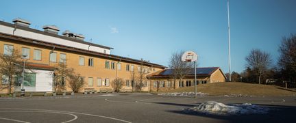 En tom basketplan framför en skolbyggnad i gult tegel.