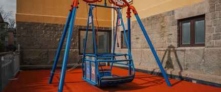 En blå gungställning som står framför en skolbyggnad.