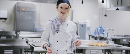 En tjej i kockkläder lagar mat i ett restaurangkök. 