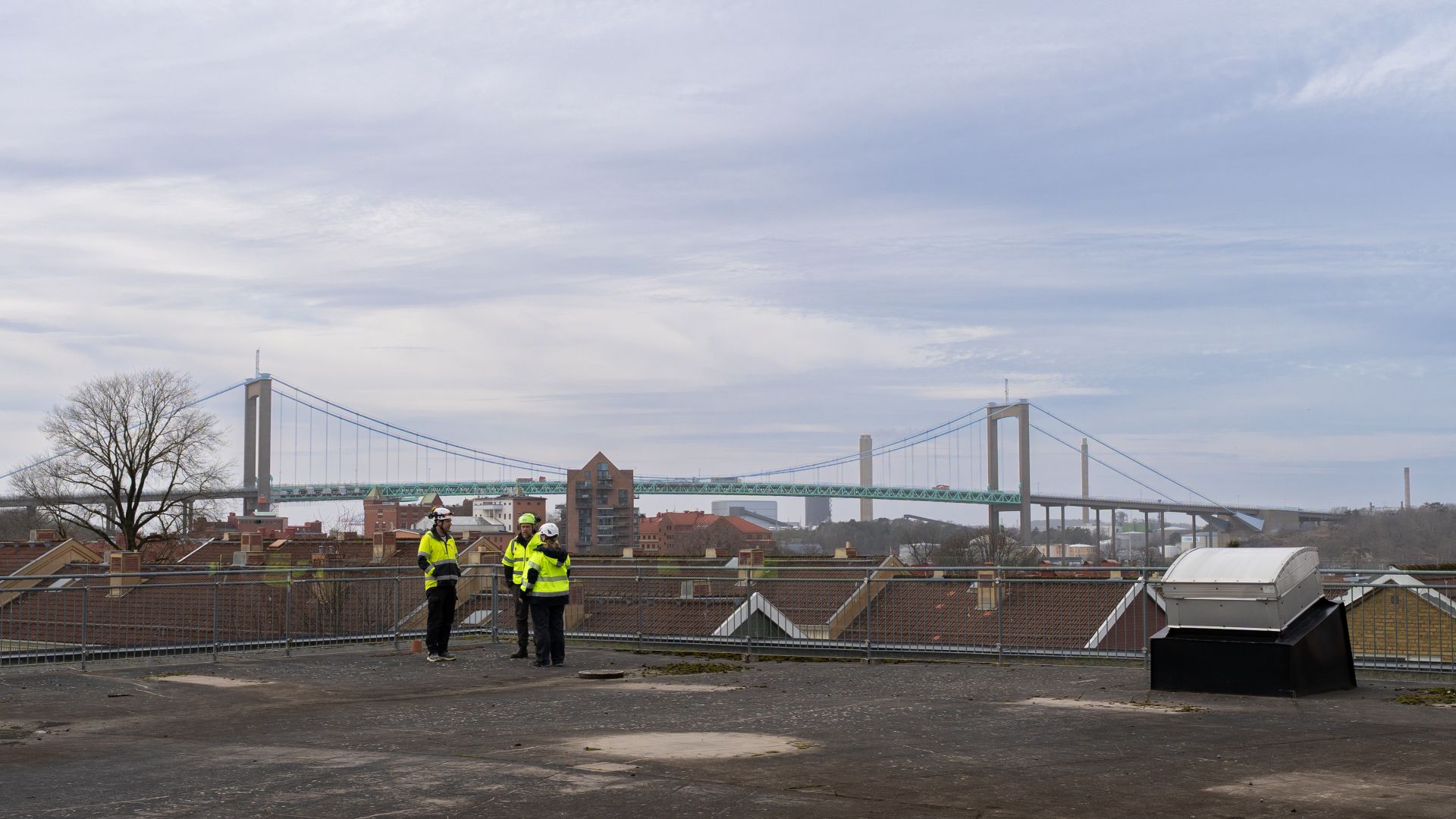 Tre personer i varselkl&auml;der och hj&auml;lm st&aring;r och pratar p&aring; en stor terrass. I bakgrunden ser man &Auml;lvsborgsbron.