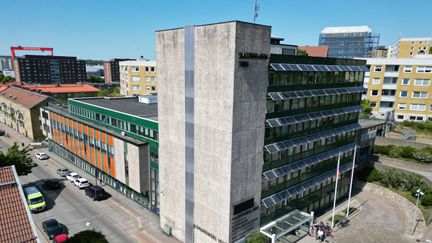 Ett högt hus med grå fasad bredvid en väg.