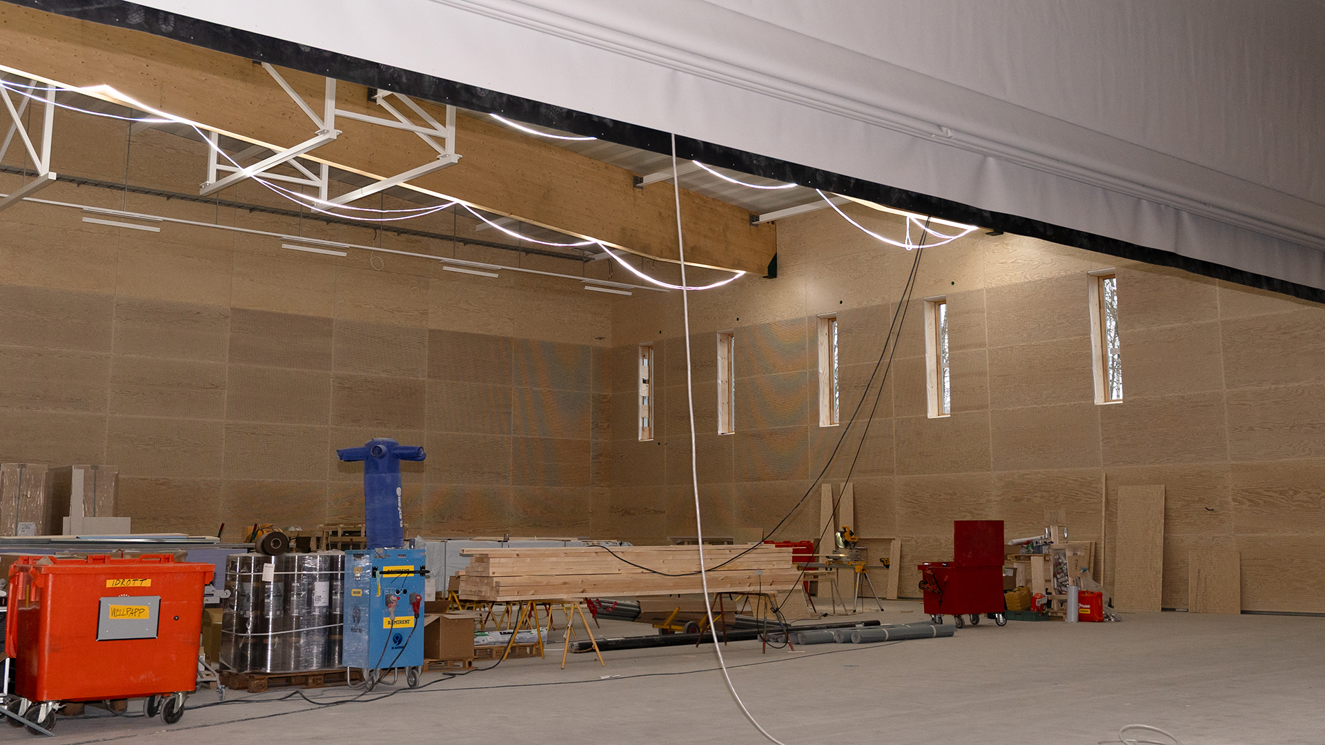 En stor, &ouml;ppen sal. Br&auml;dor och annat byggmaterial st&aring;r f&ouml;rvarat i ena delen. I taket finns en vikv&auml;gg som &auml;r halvt nerhissad.