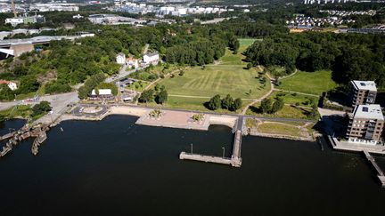 Flygfoto på park vid älven med sandstrand, pir och planteringar.