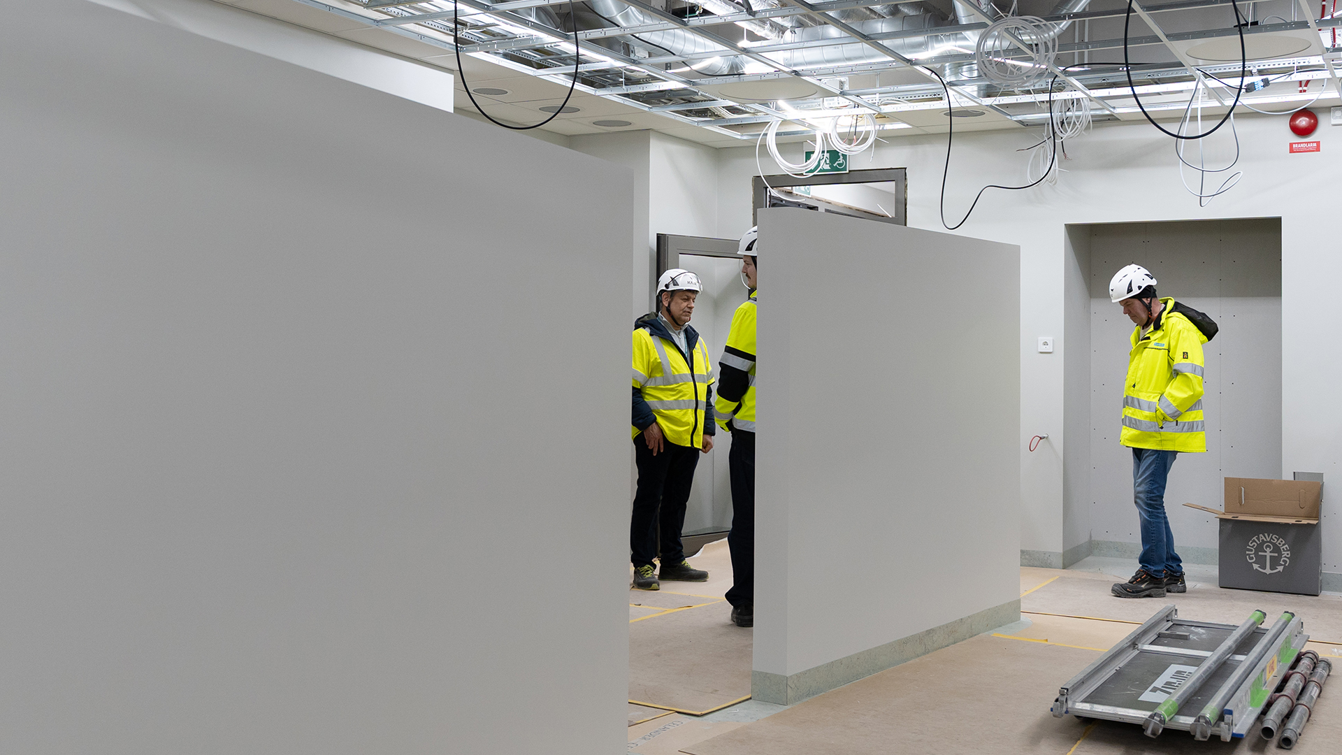 Tre personer i varselkl&auml;der och hj&auml;lm st&aring;r halvt dolda av cirka tv&aring; meter h&ouml;ga v&auml;ggar.