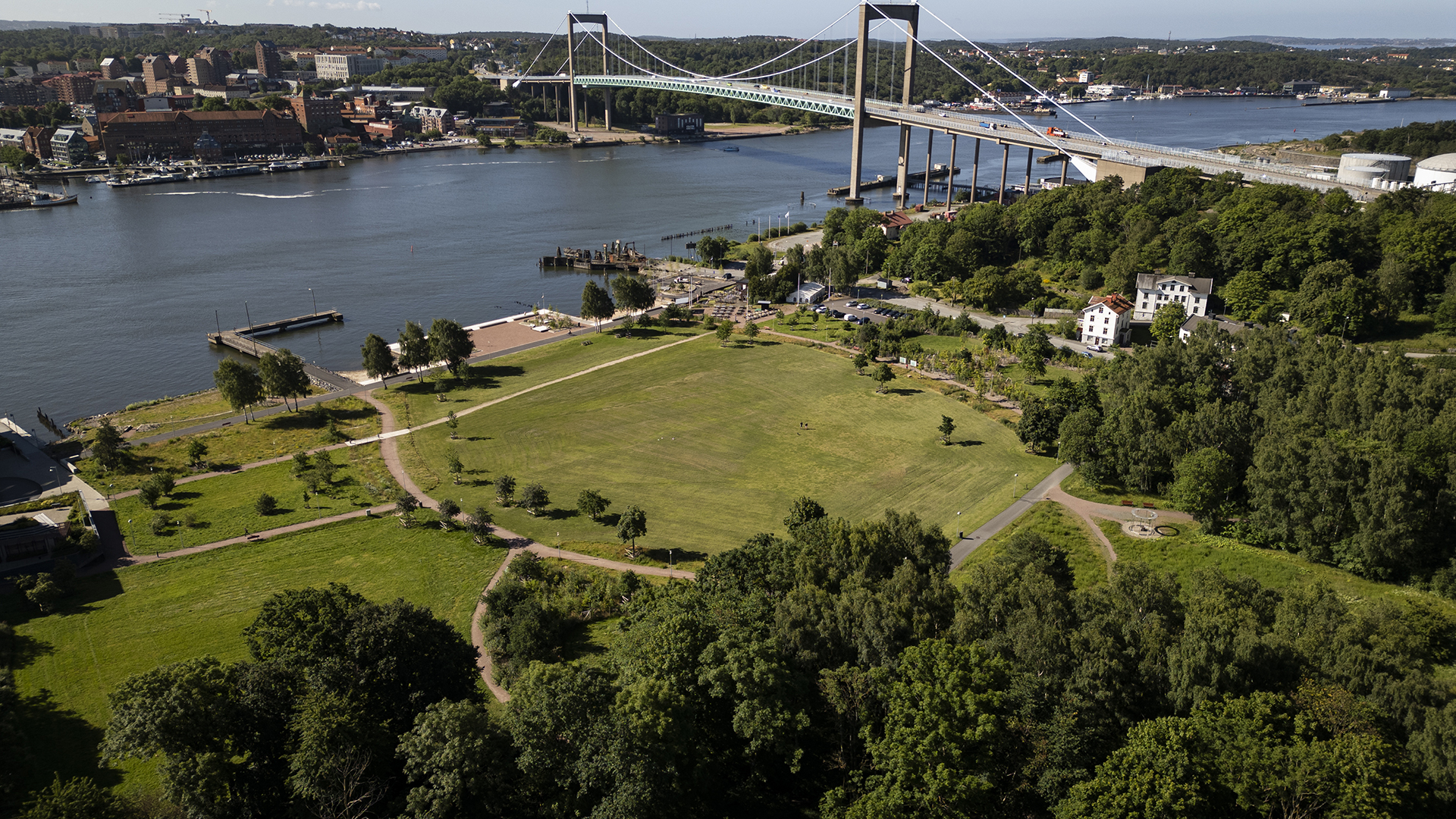 Drönarbild över den stora gräsmattan och strandlinjen mot älven i Färjenäsparken. Över älven syns Älvsborgsbron.
