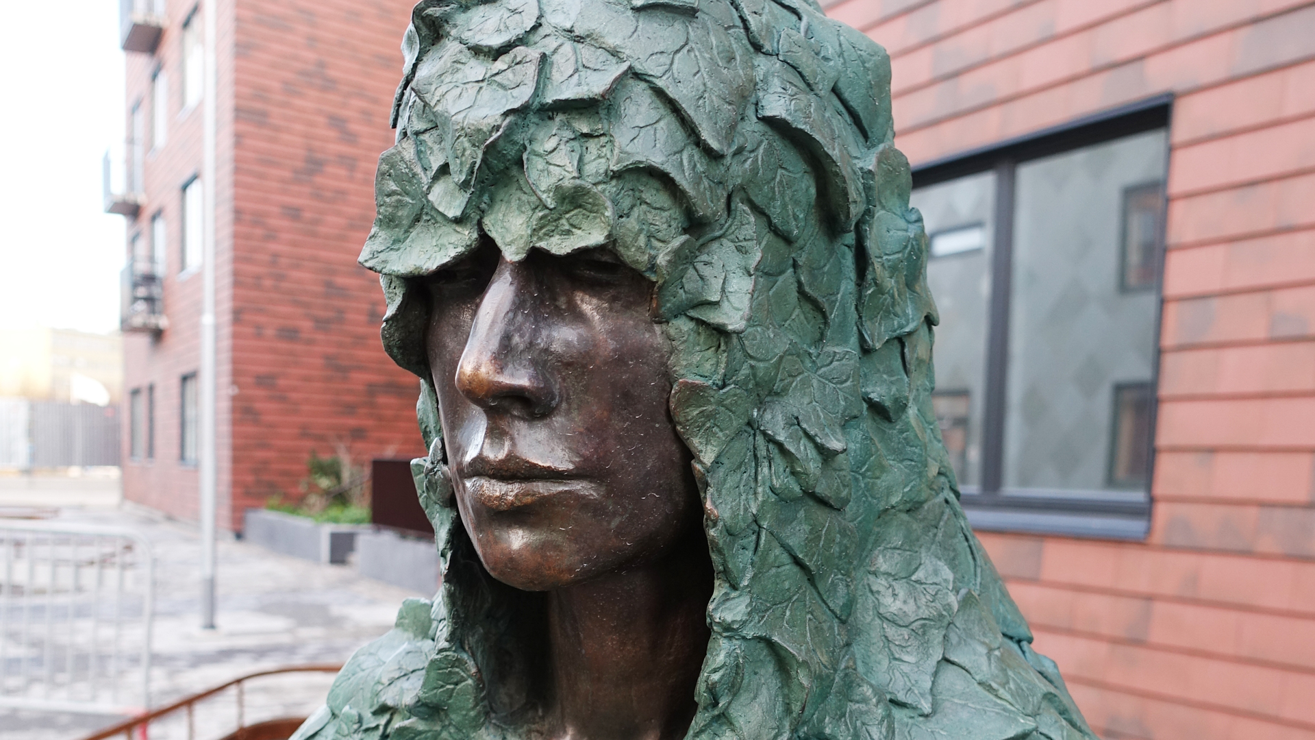 Huvudet av en bronsskulptur. Skulpturen har en huva av murgröna över huvudet.
