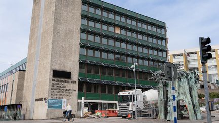 En hög betongbyggnad med många våningar. Framför står en lastbil innanför byggstaket.
