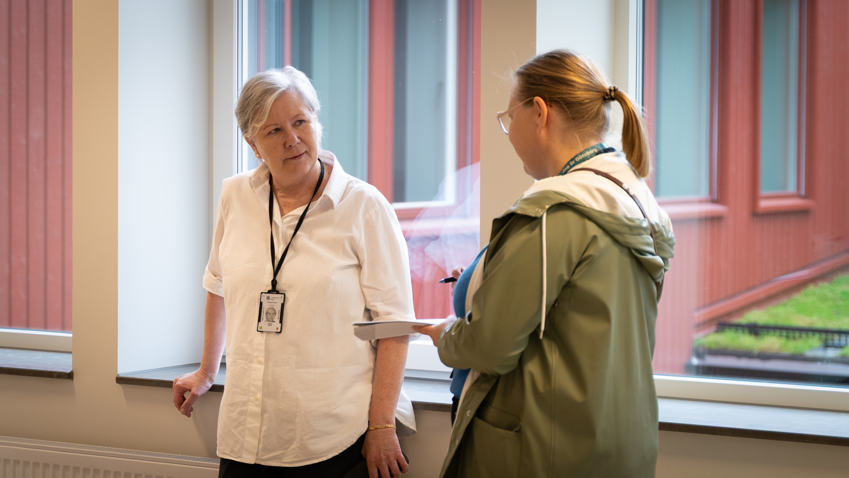 Två personer står vid ett fönster och pratar med varandra.