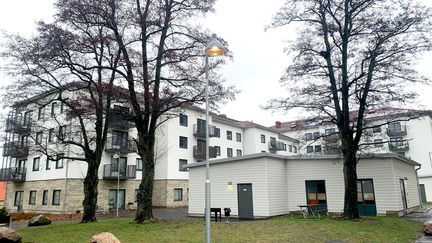 Kvarter vid Gamlestadsvägen. Flerbostadshus med tegelgrund, vit fasad och balkonger. I förgrunden ett mindre hus på innergård samt tre stora träd utan löv.