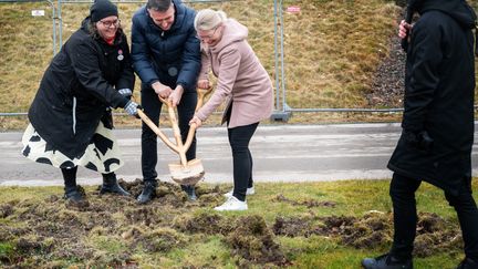 Tre personer tar tillsammans ett spadtag med en treskaftad spade.