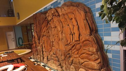 En träskulptur föreställande en klippa täcker en i övrigt kaklad vägg.