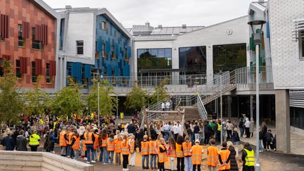 En skolgård full med elever, många i orangea västar.