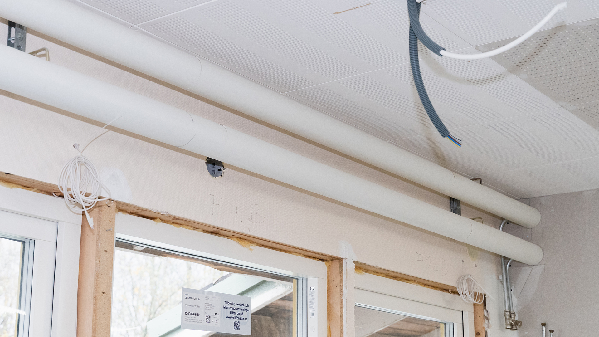 Tv&aring; r&ouml;r g&aring;r l&auml;ngs innertaket, ovanf&ouml;r f&ouml;nster. L&ouml;sa sladdar h&auml;nger ner fr&aring;n taket i f&ouml;rgrunden.