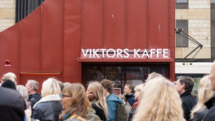 En röd byggnad med skylten Viktors kaffe på, i förgrunden en folksamling.