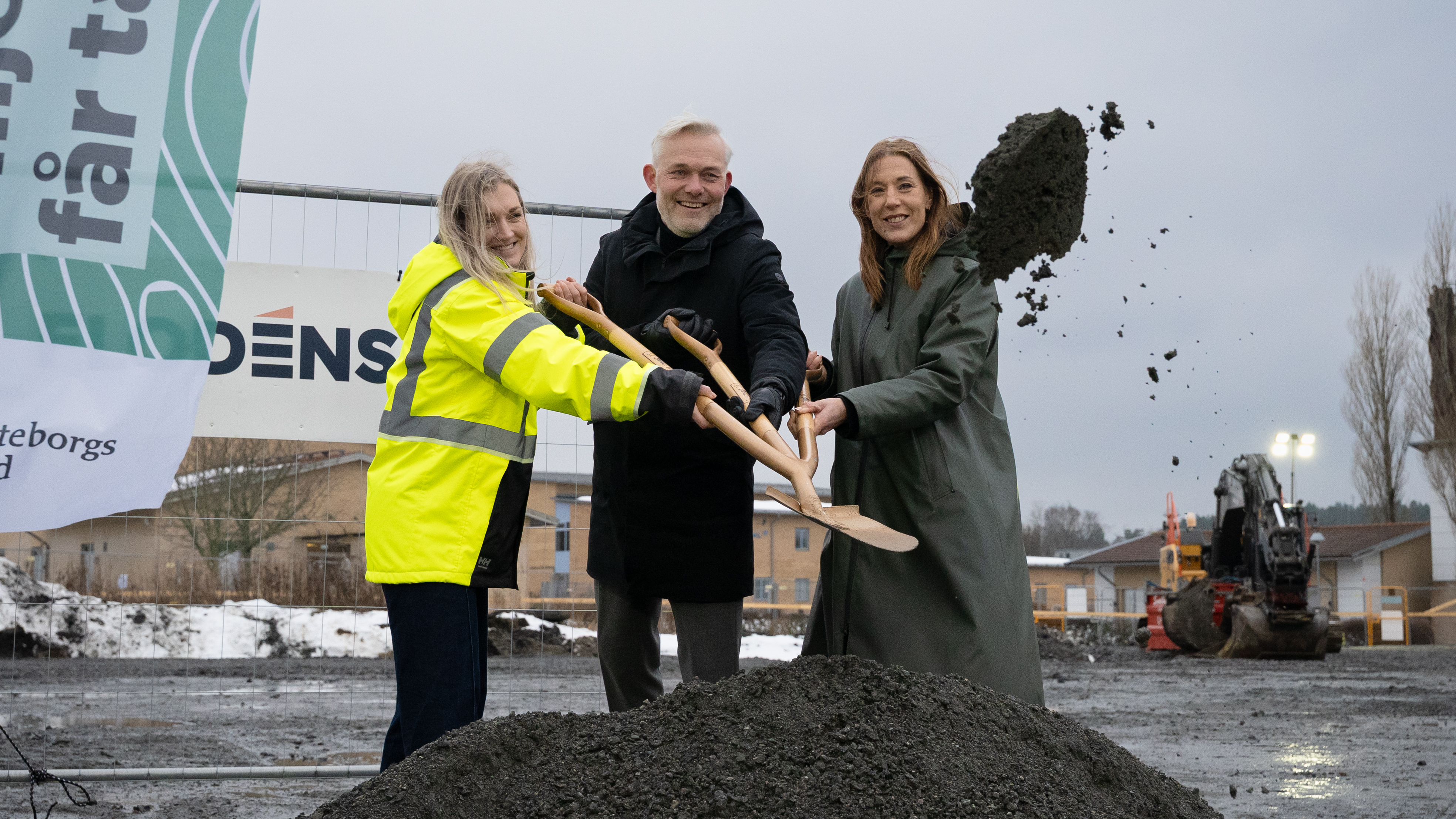 Tre personer kastar tillsammans iväg grus med en treskaftad spade.