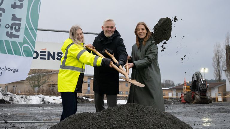 Tre personer kastar tillsammans iväg grus med en treskaftad spade.