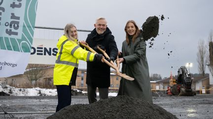 Tre personer kastar tillsammans iväg grus med en treskaftad spade.