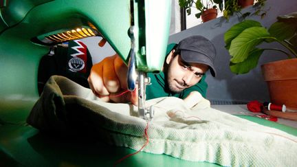  En kille med keps sitter vid en grön symaskin och syr. Runt sig har han gröna växter och trådrullar.