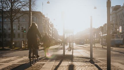 Avenyn i solsken, en trottoar, cyklist och fotgängare.