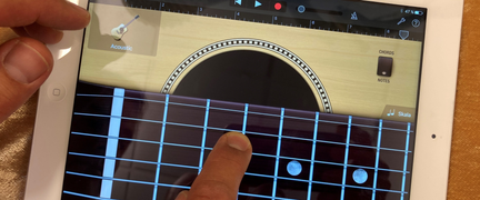 En surfplatta med appen GarageBand där man kan spela på en gitarr. Ett finger rör strängarna.