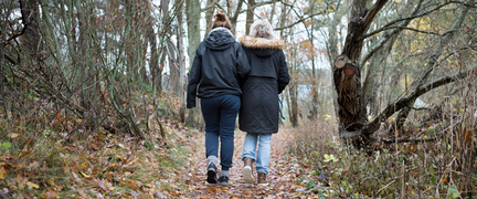 Två personer promenerar på en stig i skogen. Det är höst, träden har tappat sina blad. 