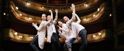 Fyra unga personer står på en scen nära varandra och klappar i händerna. I bakgrunden läktare i guld och röd sammet. De är på Stora Teatern.