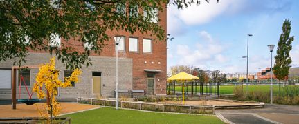 En skolgård med en gungställning och ett gult parasoll.