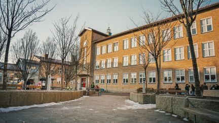 Johannebergsskolans skolgård med några personer och träd i bakgrunden.