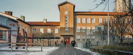 Johannebergsskolans skolgård med några personer och en lekplats i bakgrunden.