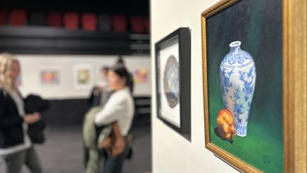 Foto från konstutställning, i bakgrunden två personer som står och pratar