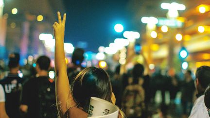 Person som gör v-tecken med ena handen. I bakgrunden en folkmassa.