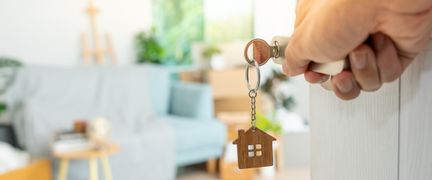 En hand öppnar en dörr och i bakgrunden syns en blå soffa.