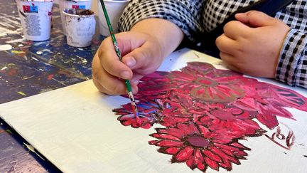 En person målar en tavla med röda blommor.
