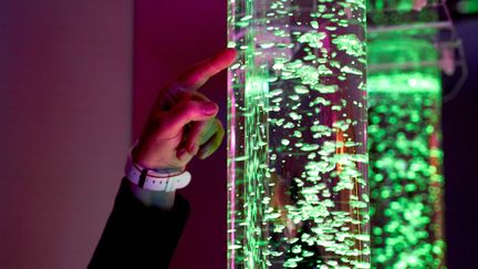 En hand pekar på ett vattenfyllt upplyst rör med bubblor.