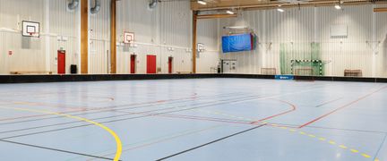 Sporthall med blått golv och ljusa väggar. I bakgrunden syns basketkorgar.