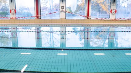 Bassängen i Askims simhall sedd från långsidan. Vattnet är stilla. Längs väggen går stora fönster.