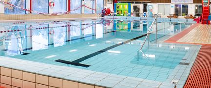 Bassängen i Askims simhall. Vattnet är stilla. Längs väggen går stora fönster.