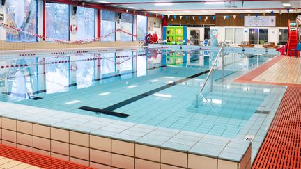 Bassängen i Askims simhall. Vattnet är stilla. Längs väggen går stora fönster.