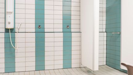 Duschrum med vitt och turkos kakel. Ett duschbås syns till höger i bilden.