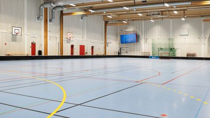 Idrottshall med blått golv. Längs väggen flera basketkorgar