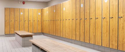 Omklädningsrum med skåp i trä och två bänkar med träskivor och bas i kakel.