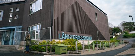 En överblick av Långedragsskolans huvudbyggnad med skolans skylt i fokus. I bakgrunden syns en person.