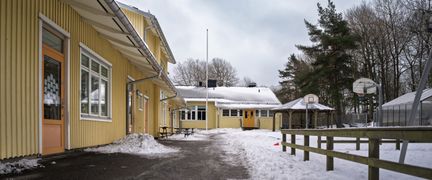 Kärrdalsskolans huvudbyggnad med några träd och ett staket i bakgrunden.