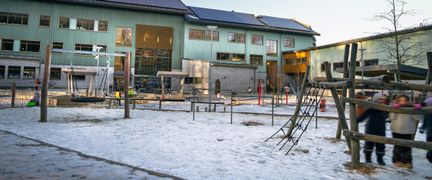 En grupp elever som står vid en lekställning på en skolgård framför en skolbyggnad.