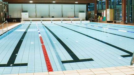 Bassängen i Kärra simhall. Vattnet är stilla. I taket syns mörka träbalkar.